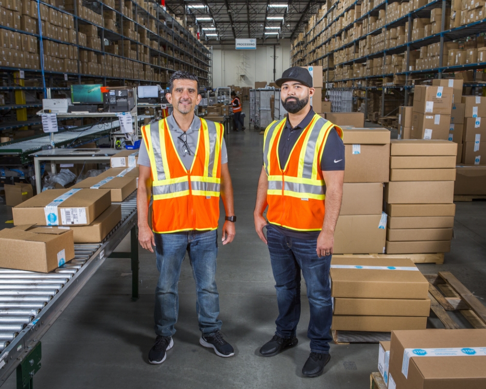Two warehouse employees in orange hi-vis vests